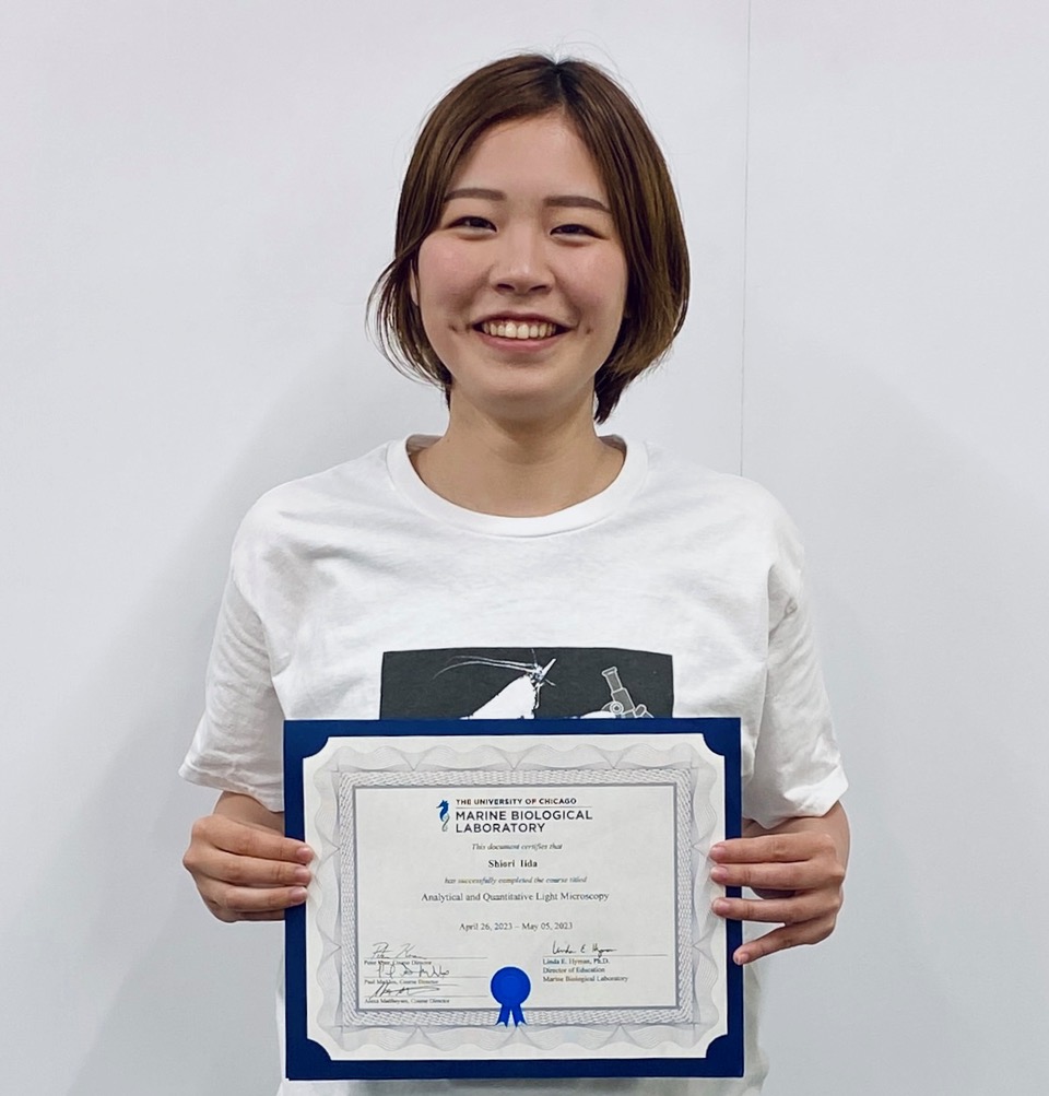 Shiori Iida with her course certificate. She is wearing a T-shirt of Analytical and Quantitative Light Microscopy 2023 with an illustration of a lobster and a microscope.